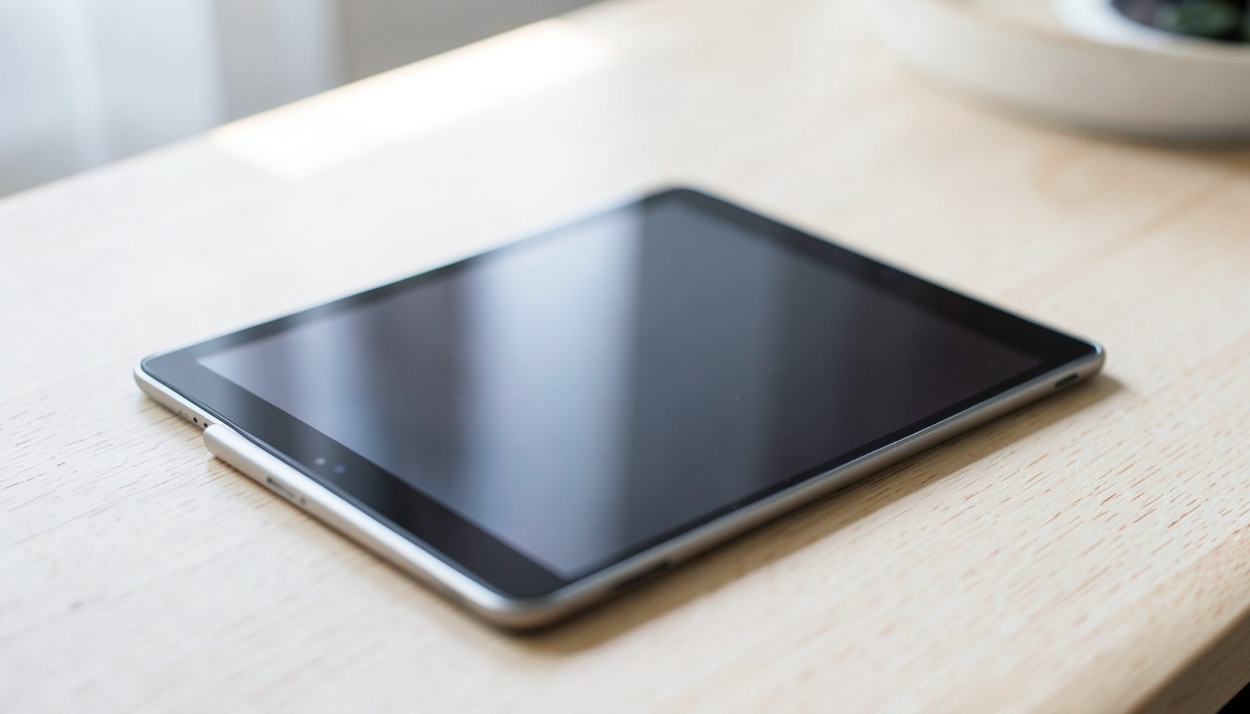 Close-up of a tablet and stylus on a pale wood desk in natural light